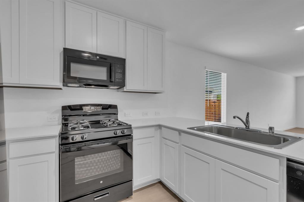 11325 Rodeo Drive Providence Village, TX 76227 - Photo 14 of 40 a kitchen with white cabinets and black appliances