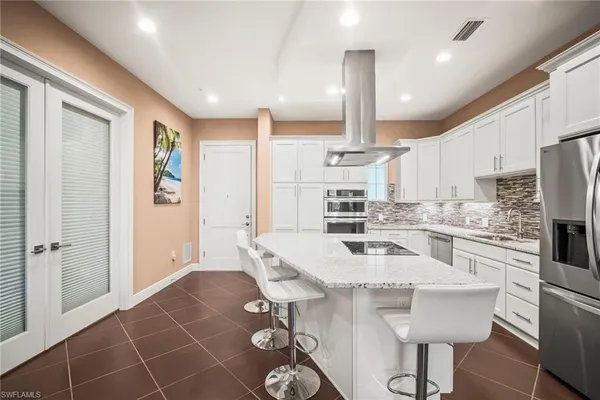 a kitchen with stainless steel appliances kitchen island granite countertop a refrigerator a stove a sink and white cabinets with wooden floor