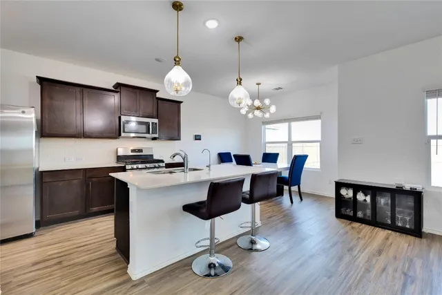 a open kitchen with stainless steel appliances granite countertop a stove a refrigerator a kitchen island a dining table and chairs with wooden floor