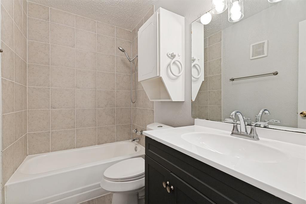 5522 Boca Raton Boulevard, Unit 404 Fort Worth, TX 76112 - Photo 10 of 12 Full bathroom featuring a white tub, light-toned tile surround, a built-in white storage cabinet, and a vanity with a dark cabinet base, white countertop, and integrated sink