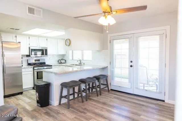 a kitchen with stainless steel appliances granite countertop a refrigerator a sink dishwasher a stove with white cabinets and wooden floor