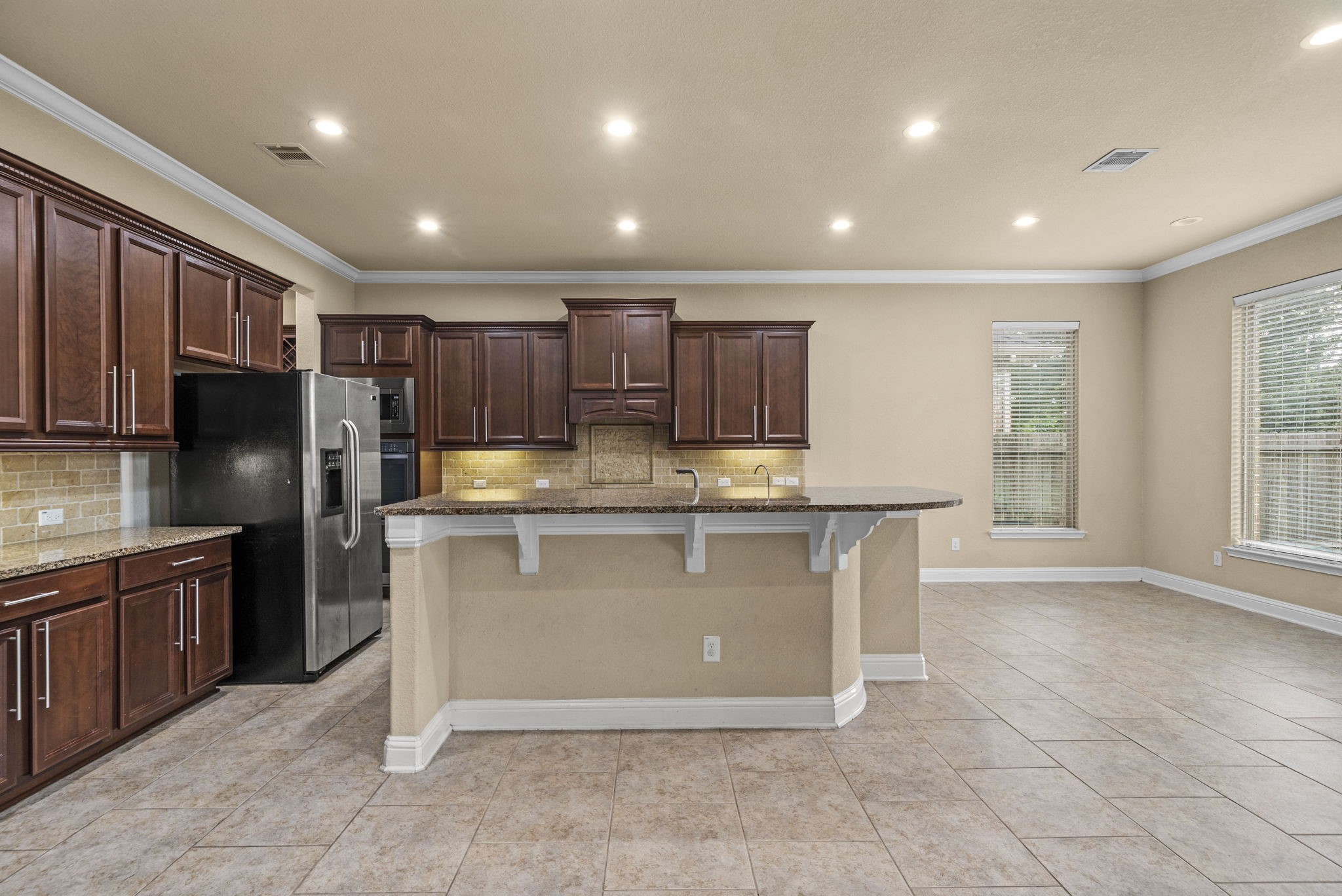 14215 Spindle Arbor Road Cypress, TX 77429 - Photo 15 of 47 This spacious kitchen features rich wood cabinetry, a large central island with a breakfast bar, stainless steel appliances, and ample natural light from large windows, creating a warm and inviting atmosphere.