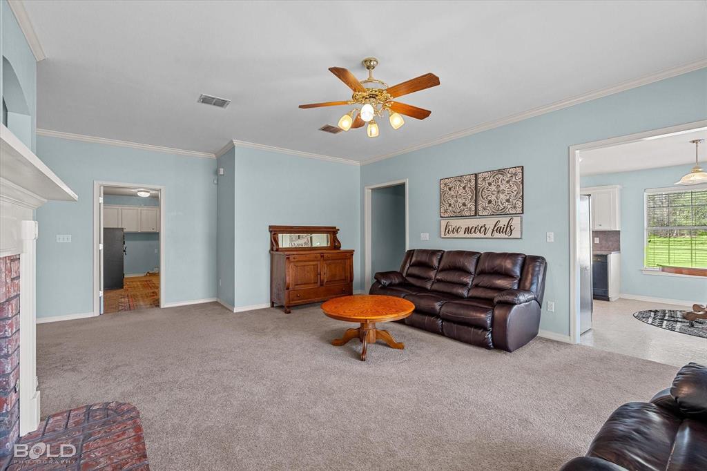 136 Scarborough Road Benton, LA 71006 - Photo 11 of 37 Carpeted living area featuring light blue walls, white crown molding, a ceiling fan with light fixture, and a brick fireplace