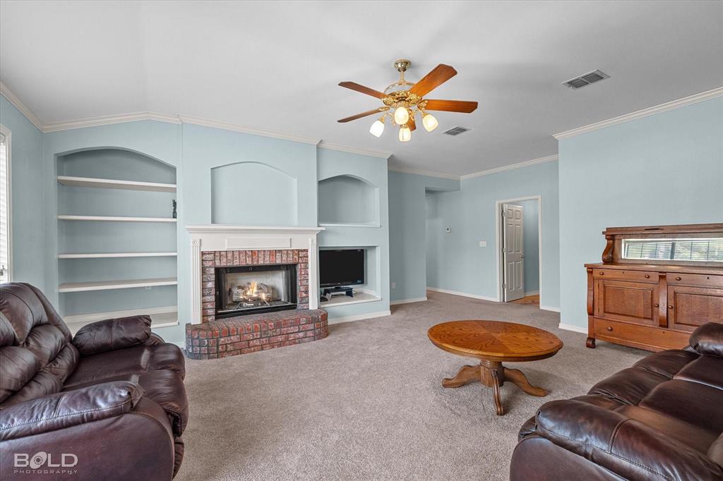 136 Scarborough Road Benton, LA 71006 - Photo 12 of 37 Living area featuring a brick fireplace with a white mantel, built-in shelving, a ceiling fan with integrated lighting, and carpeted flooring