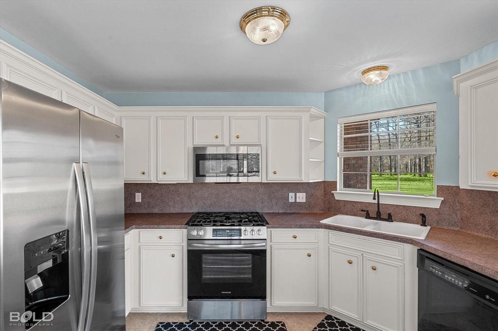 136 Scarborough Road Benton, LA 71006 - Photo 15 of 37 Kitchen featuring white cabinetry, stainless steel appliances, a double basin sink with a black faucet, and a window overlooking exterior greenery
