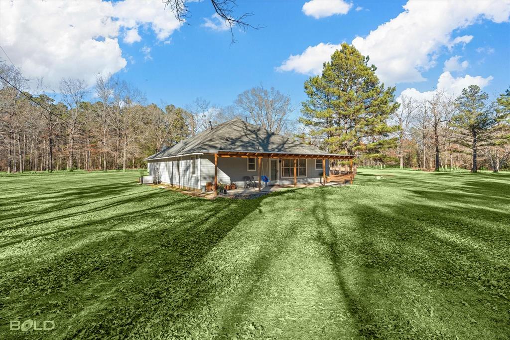 136 Scarborough Road Benton, LA 71006 - Photo 34 of 37 Expansive green lawn surrounds this property, featuring a covered patio with exposed wood posts and a gray shingled roof