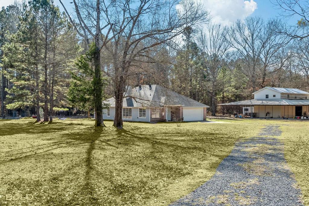 136 Scarborough Road Benton, LA 71006 - Photo 36 of 37 Spacious property featuring a light-colored main residence with an attached garage, a separate large outbuilding with an upper level, a gravel driveway, mature trees, and an expansive lawn