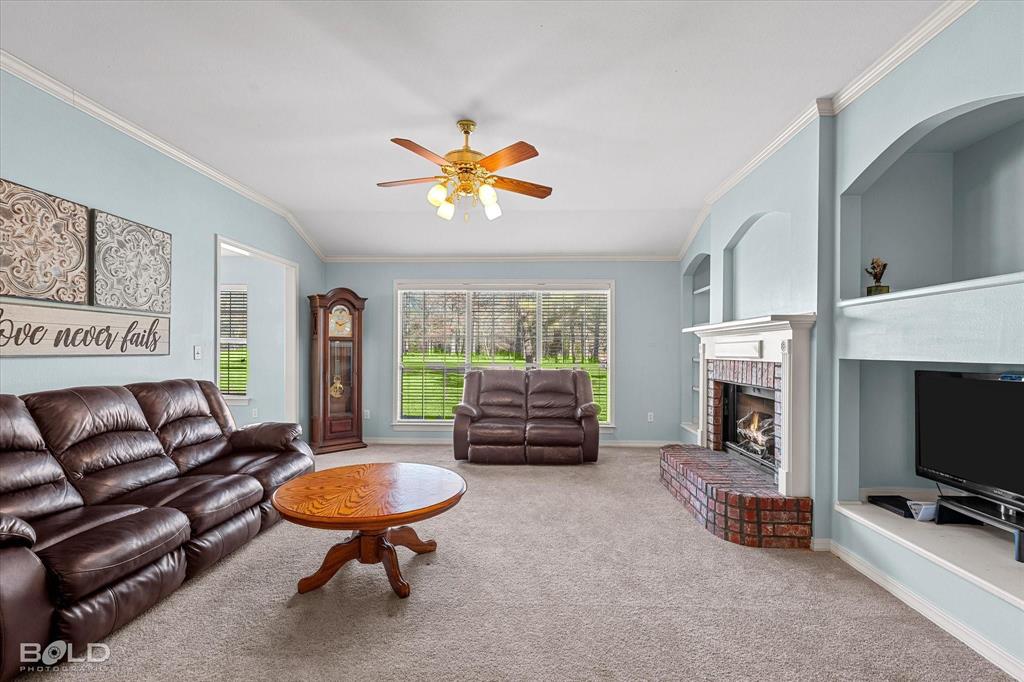 136 Scarborough Road Benton, LA 71006 - Photo 8 of 37 Living room featuring a brick fireplace with a white mantel, built-in shelving, a ceiling fan with integrated lighting, and multiple windows overlooking green space