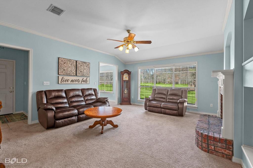 136 Scarborough Road Benton, LA 71006 - Photo 9 of 37 Spacious living area featuring vaulted ceilings, a ceiling fan with integrated lighting, large windows, an arched entryway, and a brick fireplace with a white mantel
