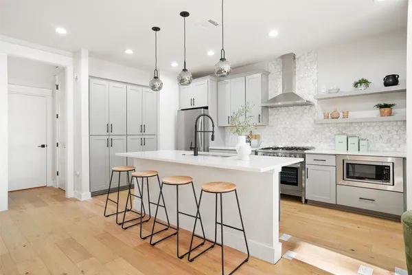 a kitchen with stainless steel appliances granite countertop a stove a sink a refrigerator and white cabinets with wooden floor