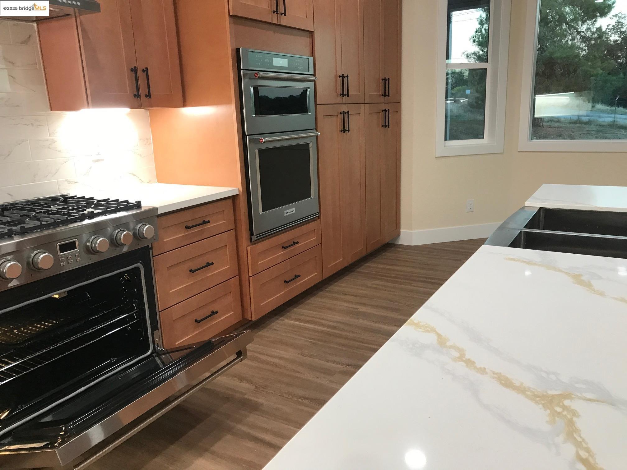 17500 Harvard Mine Road Jamestown, CA 95327 - Photo 7 of 28 Kitchen featuring stainless steel appliances, light stone countertops, dark wood-type flooring, tasteful backsplash, and brown cabinets