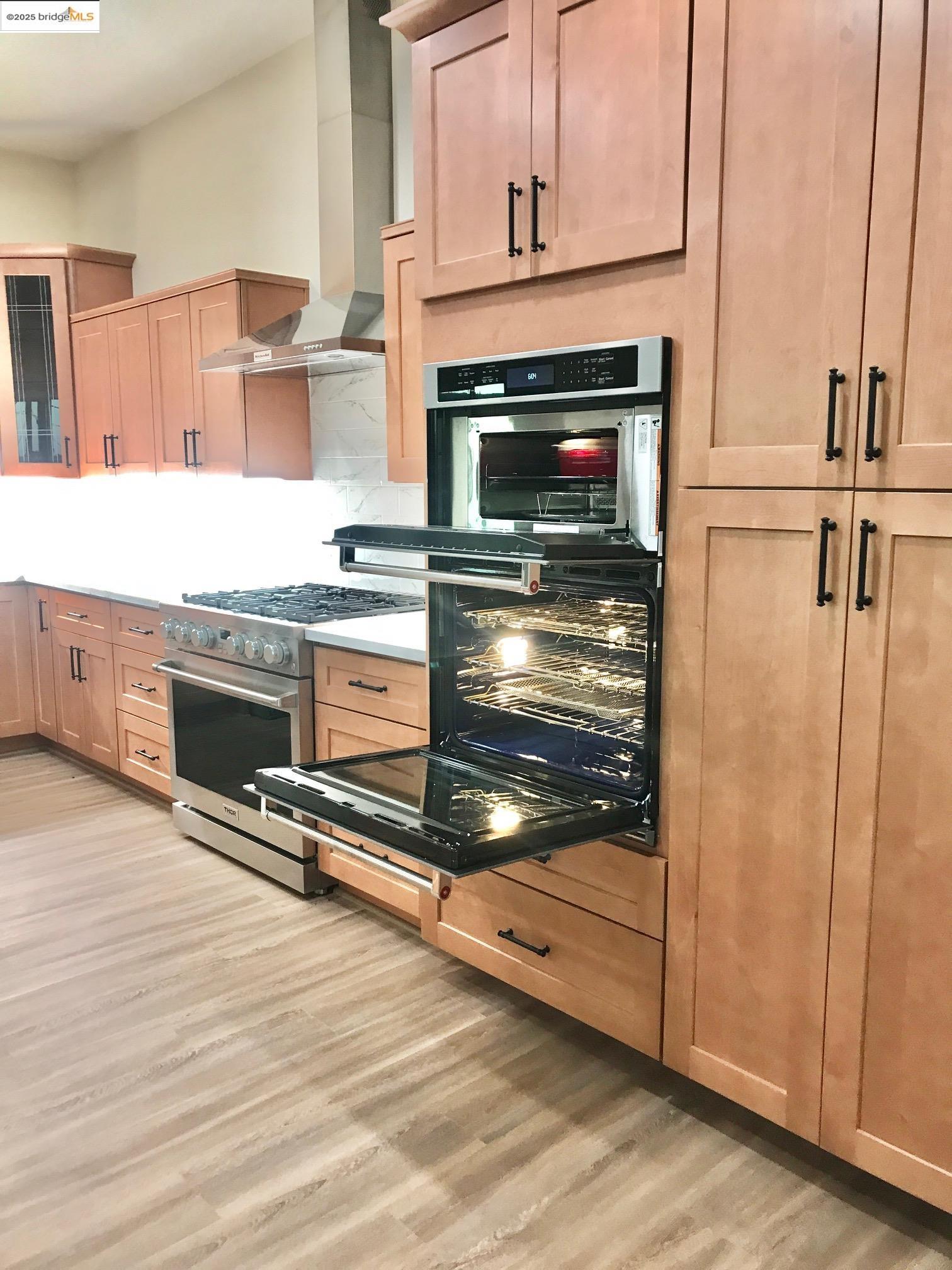 17500 Harvard Mine Road Jamestown, CA 95327 - Photo 9 of 28 Kitchen featuring wall chimney exhaust hood, light brown cabinetry, stainless steel range with gas cooktop, multiple ovens, and glass insert cabinets