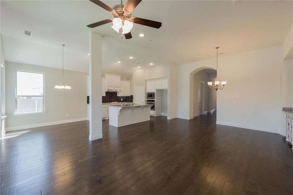 867 Forest Street Little Elm, TX 76227 - Photo 13 of 22 an empty room with wooden floor a ceiling fan and kitchen view