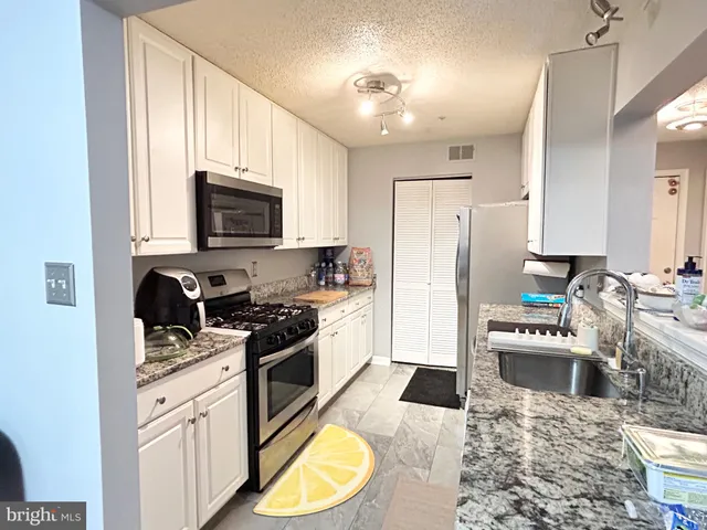 a kitchen with stainless steel appliances granite countertop a refrigerator a stove top oven a sink dishwasher and white cabinets with wooden floor