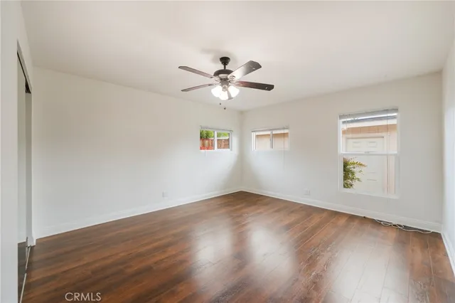 an empty room with wooden floor chandelier fan and windows