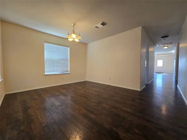 an empty room with wooden floor chandelier and windows