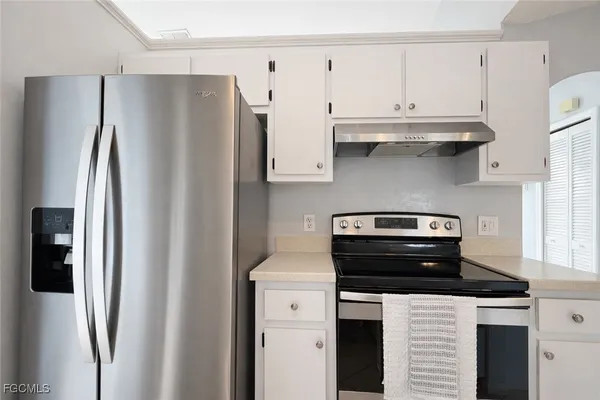 a kitchen with stainless steel appliances kitchen island granite countertop a stove a sink a refrigerator and white cabinets with wooden floor
