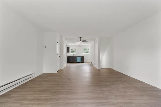 a view of empty room with wooden floor and kitchen