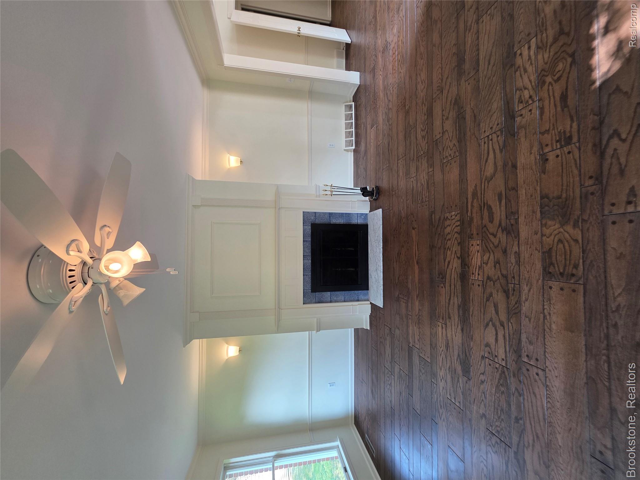 1210 Springborrow Drive Flint, MI 48532 - Photo 12 of 34 Wood-finish flooring throughout, featuring a fireplace with a tiled surround and hearth, white mantel, and integrated wall sconces