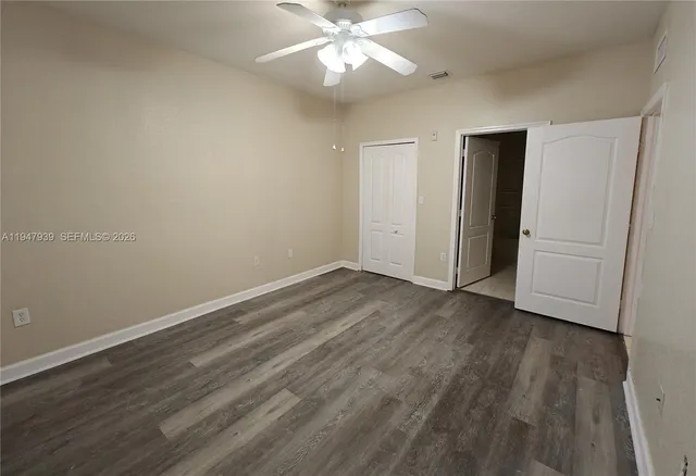 a view of an empty room with wooden floor and a ceiling fan