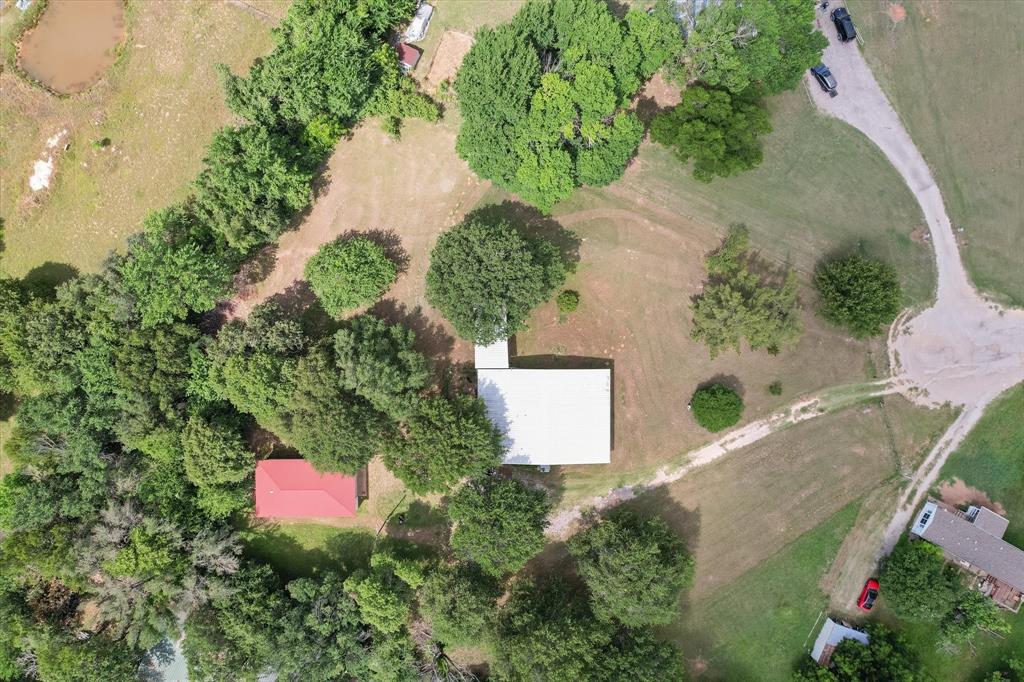 126 Smallwood Court Springtown, TX 76082 - Photo 23 of 24 Expansive property featuring a white-roofed structure, a red-roofed outbuilding, mature trees, open grassy areas, and a natural pond