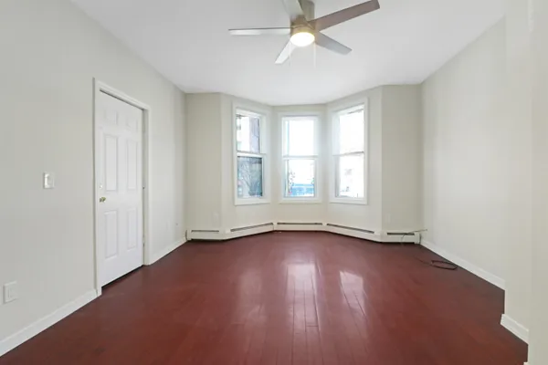 an empty room with wooden floor fan and windows