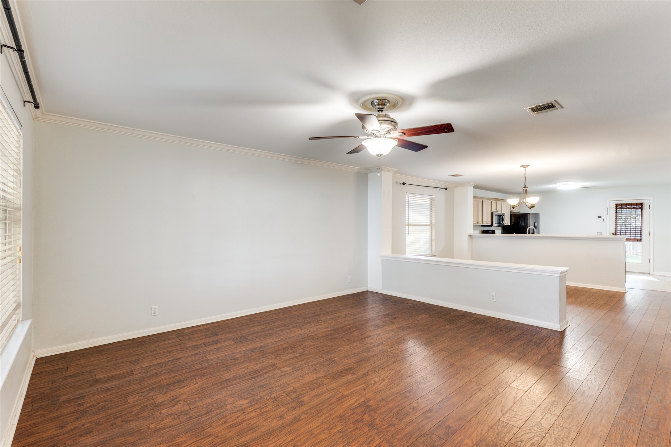 272 Tobin Drive Buda, TX 78610 - Photo 13 of 25 Unfurnished living room featuring dark wood-style flooring, a chandelier, ceiling fan, and crown molding