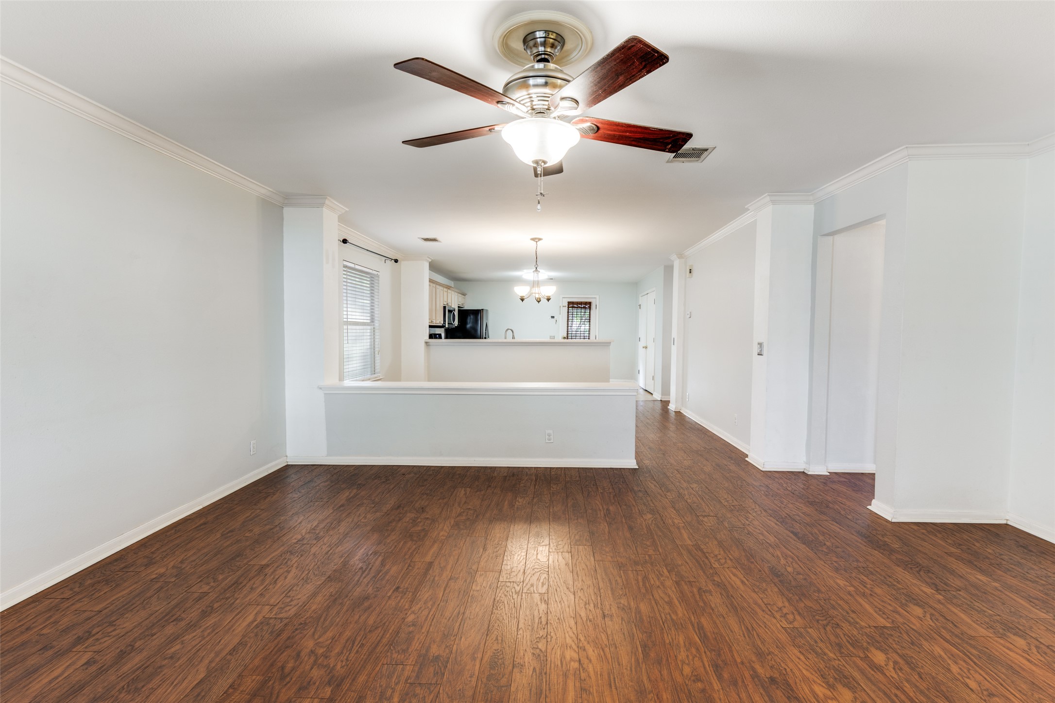 272 Tobin Drive Buda, TX 78610 - Photo 14 of 25 Unfurnished living room with ornamental molding, dark wood-style flooring, a ceiling fan, and suspended lighting