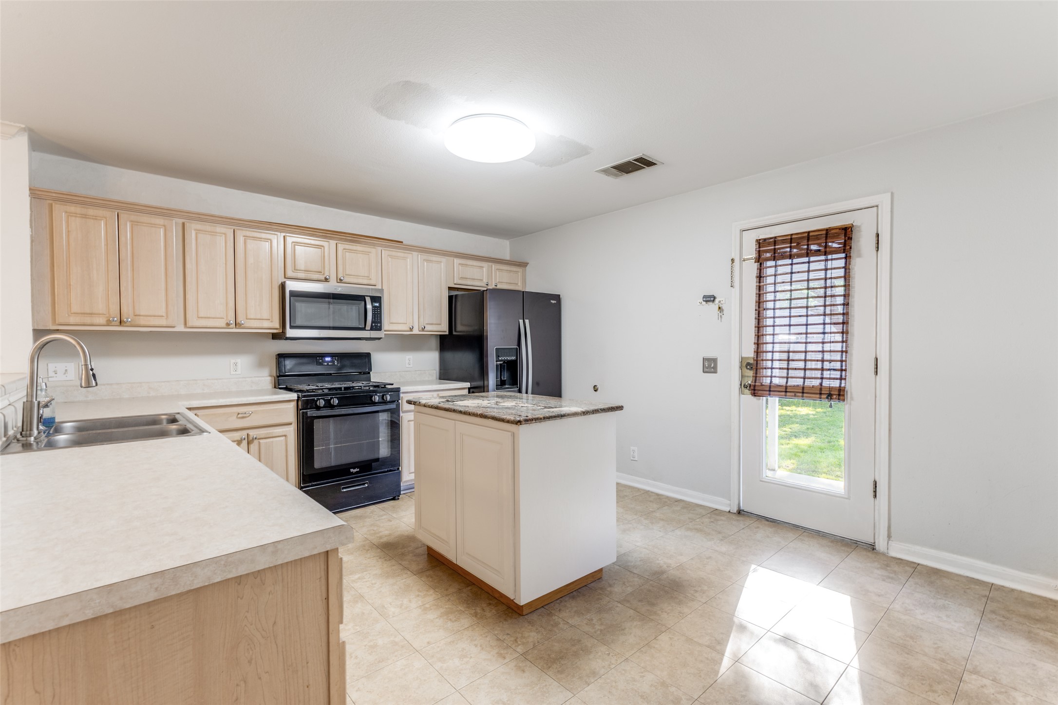 272 Tobin Drive Buda, TX 78610 - Photo 4 of 25 Kitchen featuring black appliances, light countertops, light wood finish cabinets, and a center island