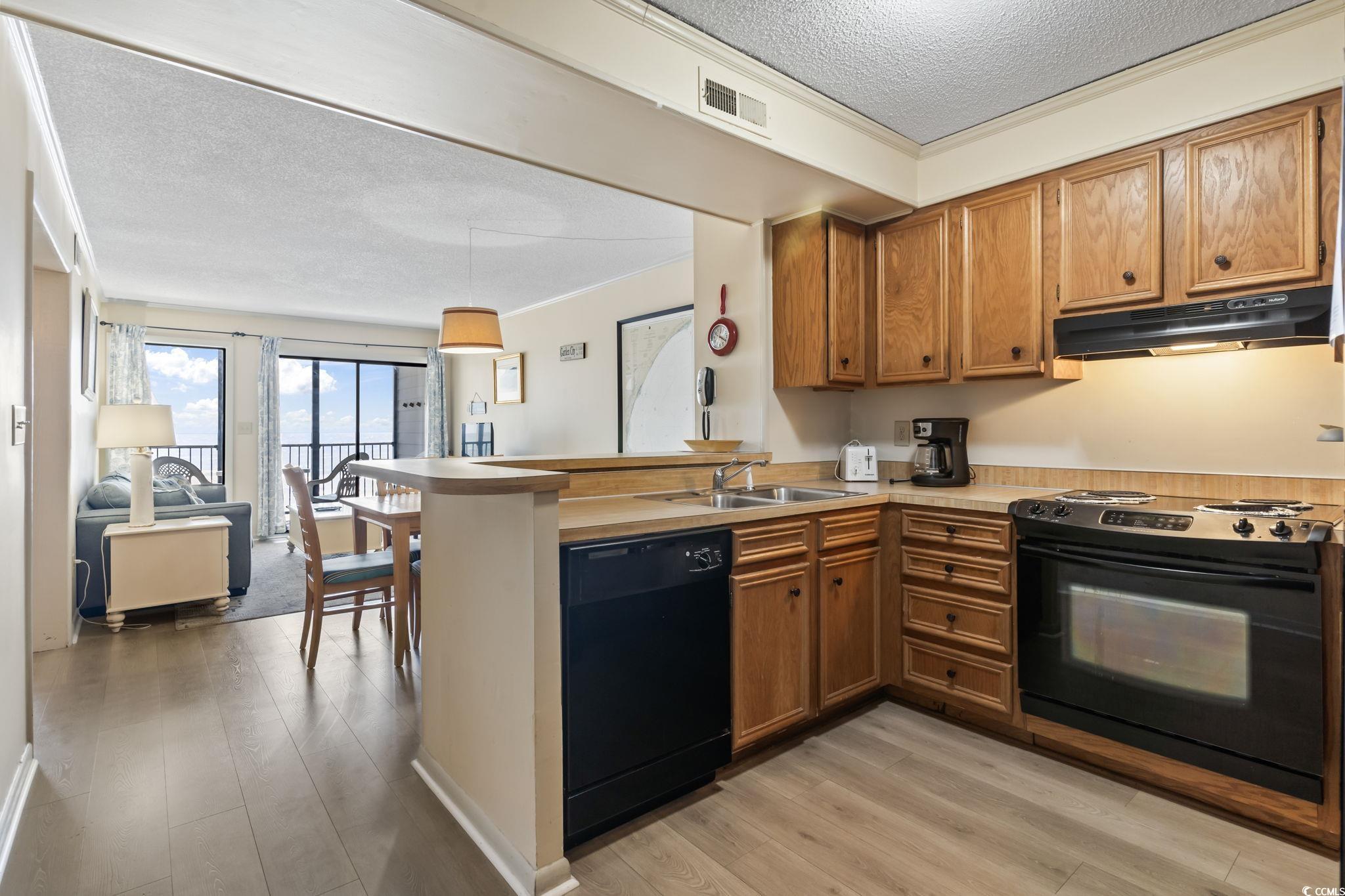 1780 North Waccamaw Drive, Unit 109 Murrells Inlet, SC 29576 - Photo 11 of 19 Kitchen featuring black appliances, a textured ceiling, light countertops, ornamental molding, and brown cabinetry