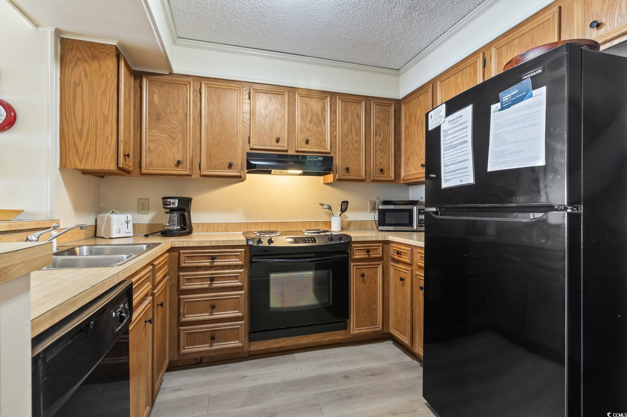 1780 North Waccamaw Drive, Unit 109 Murrells Inlet, SC 29576 - Photo 12 of 19 Kitchen featuring black appliances, light countertops, a textured ceiling, brown cabinetry, and light wood-style flooring