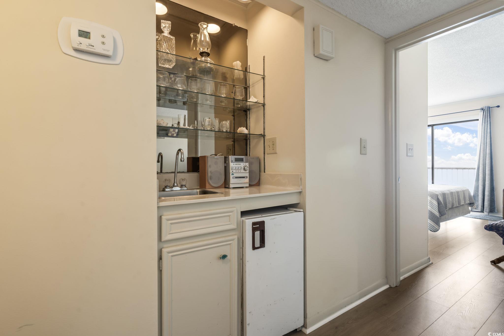 1780 North Waccamaw Drive, Unit 109 Murrells Inlet, SC 29576 - Photo 8 of 19 Indoor wet bar with white fridge, wood finished floors, white cabinetry, cream cabinetry, and a textured ceiling