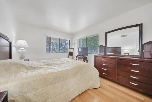 a bedroom with a bed and a large mirror on dresser next to a window