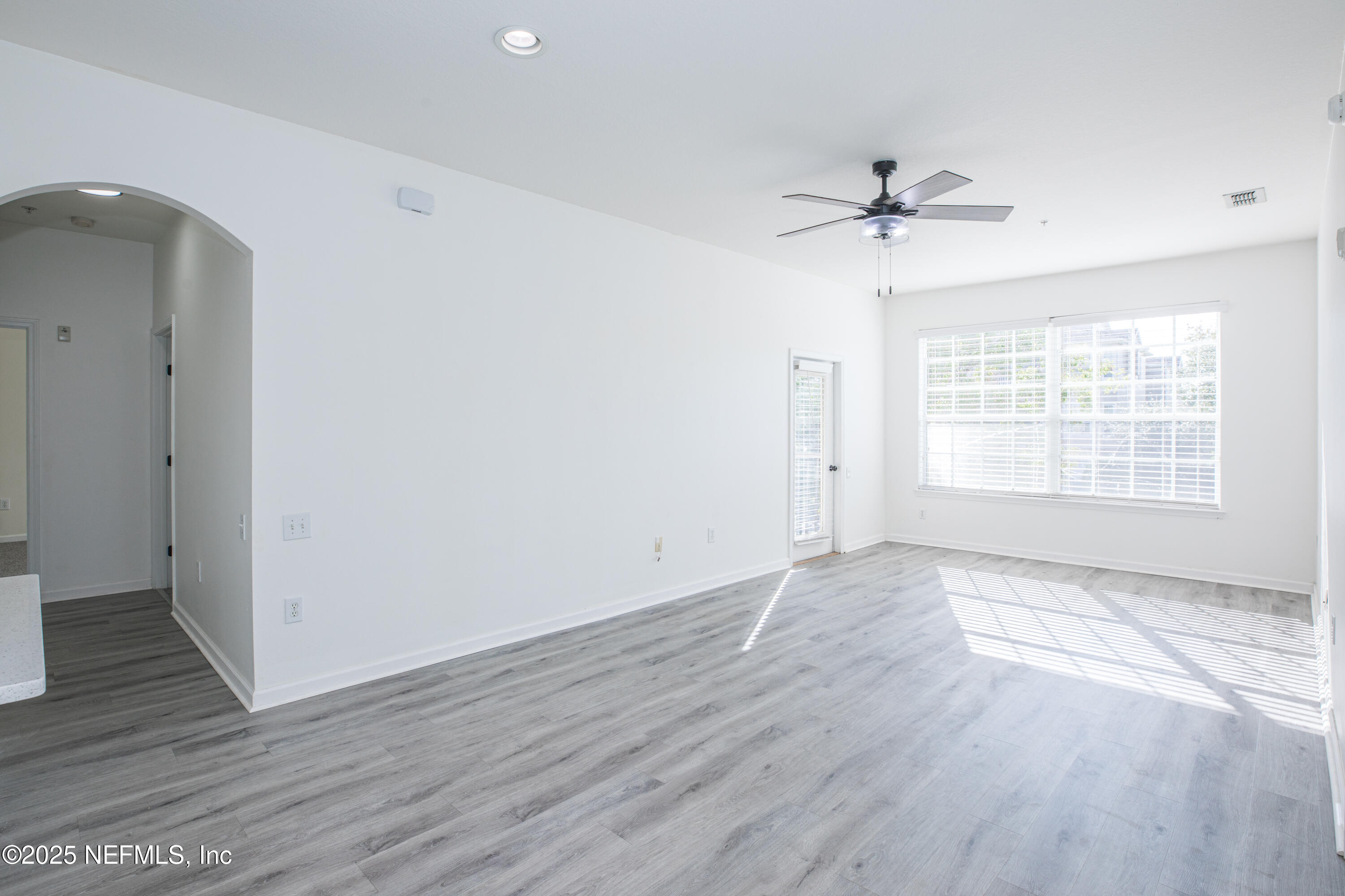 an empty room with wooden floor ceiling fan and windows