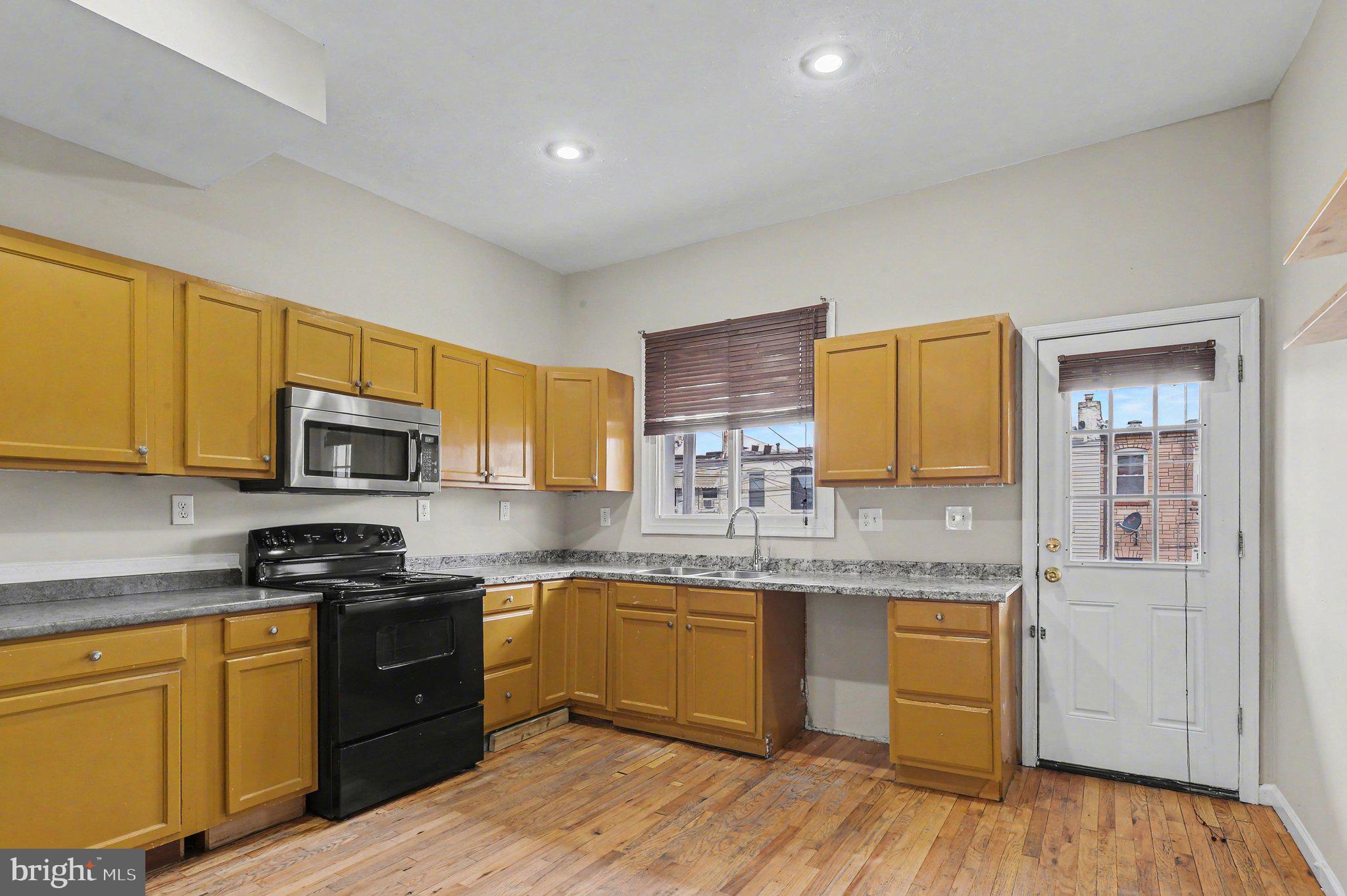 3418 East Baltimore Street Baltimore, MD 21224 - Photo 11 of 40 a kitchen with stainless steel appliances granite countertop a stove top oven a sink dishwasher and white cabinets with wooden floor