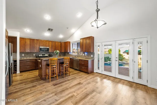 a kitchen with stainless steel appliances kitchen island granite countertop a refrigerator a oven a sink with island and chairs