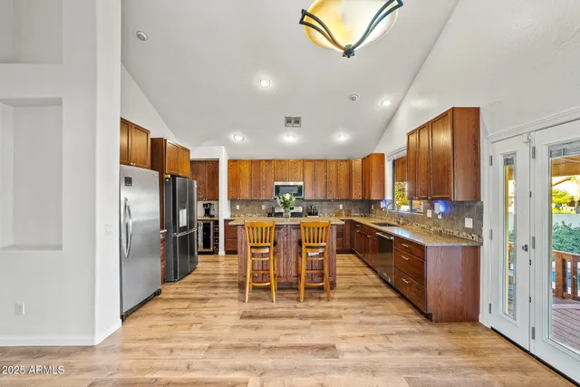 a kitchen with stainless steel appliances kitchen island granite countertop a refrigerator a stove a sink a dining table and chairs with wooden floor