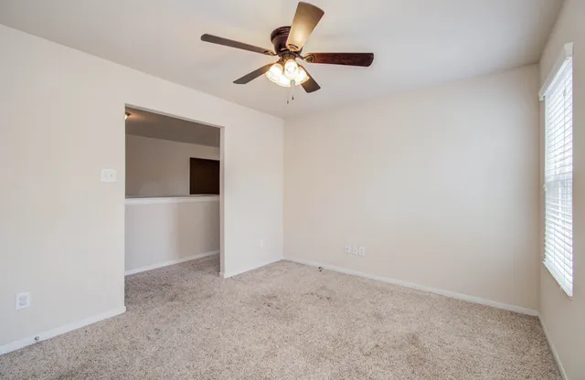 a view of an empty room with chandelier fan and a window