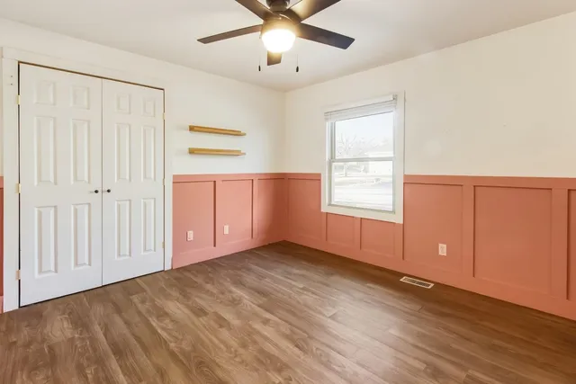 an empty room with wooden floor chandelier fan and windows