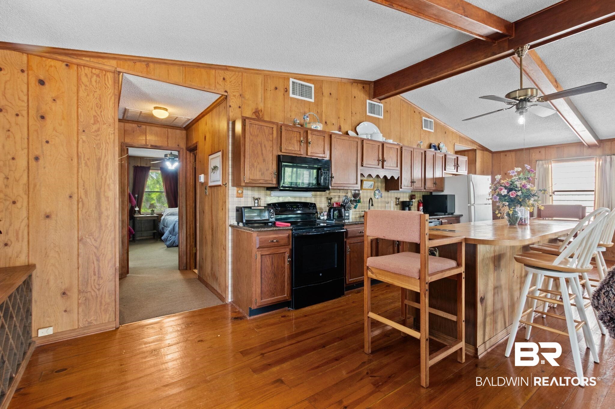 8153 Bryant's Lndg Road Stockton, AL 36579 - Photo 22 of 87 Kitchen featuring wood-finish flooring, wood paneling, wood cabinetry, a breakfast bar, and vaulted ceilings with exposed wood beams
