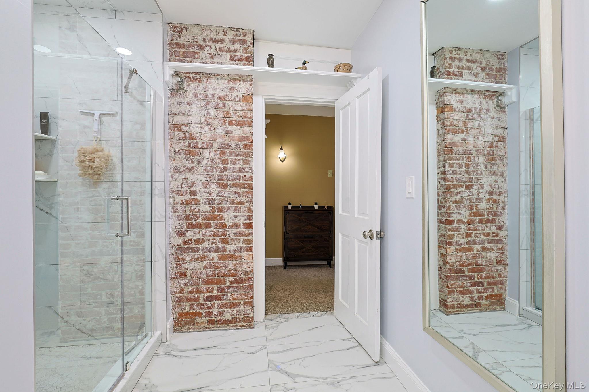 9 Library Road Tuxedo Park, NY 10987 - Photo 13 of 37 Modern bathroom with white marble-look tile flooring, a clear glass shower enclosure, and an exposed brick feature wall