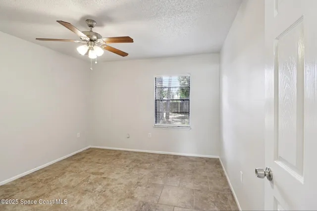 an empty room with a chandelier fan and windows