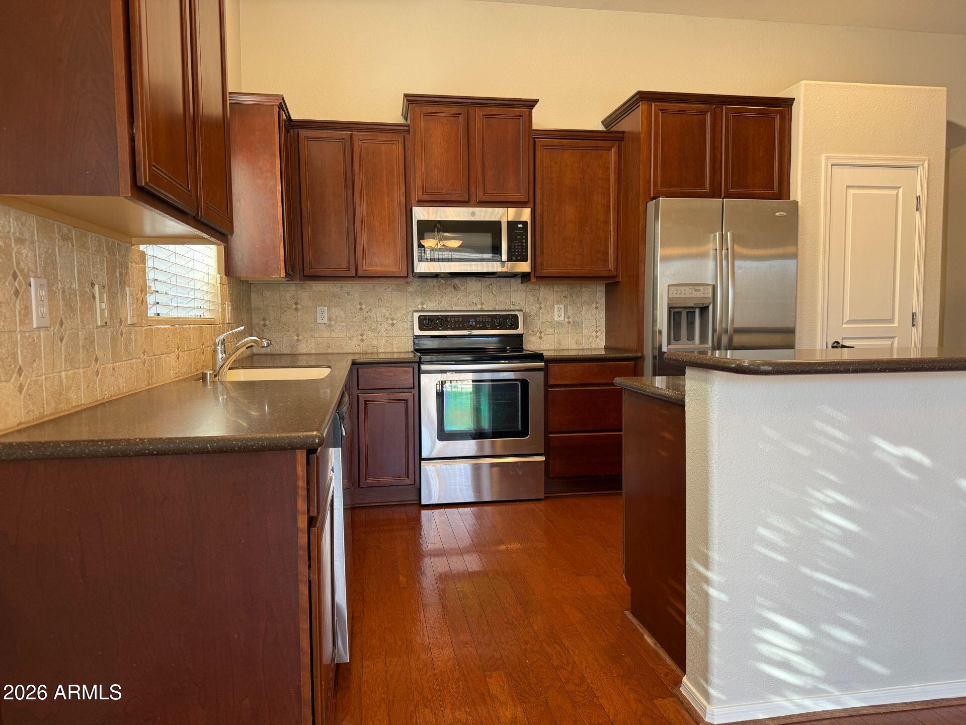 14641 West Hearn Road Surprise, AZ 85379 - Photo 12 of 42 a kitchen with stainless steel appliances granite countertop a refrigerator a stove and a sink with wooden cabinets