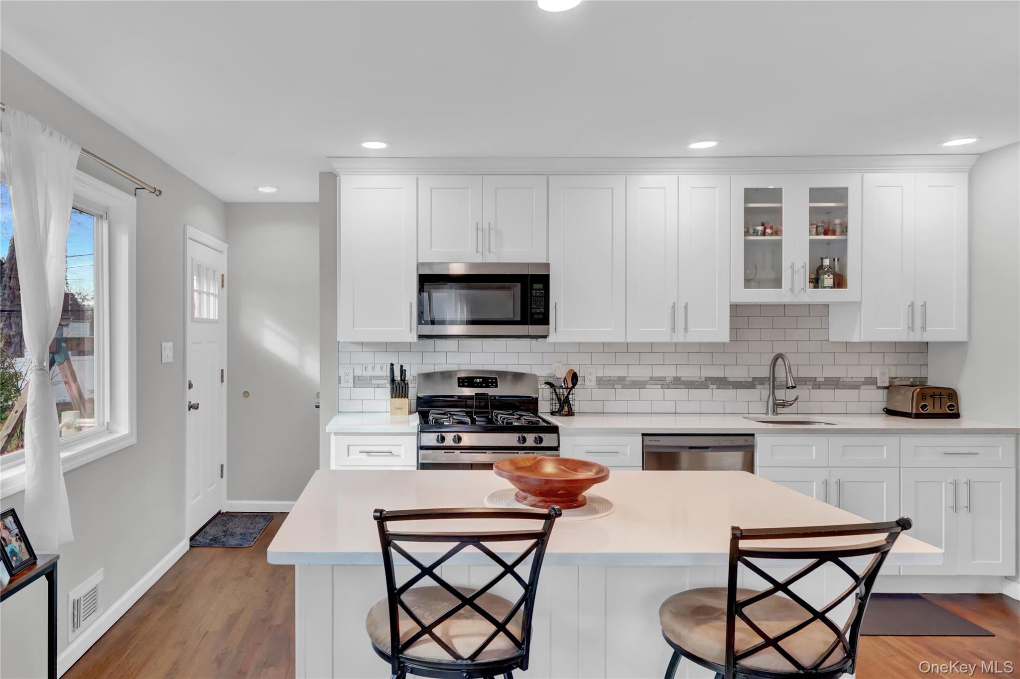 7 Winston Road Centereach, NY 11720 - Photo 11 of 18 a kitchen with stainless steel appliances kitchen island granite countertop a stove a sink a microwave a dining table and chairs with wooden floor