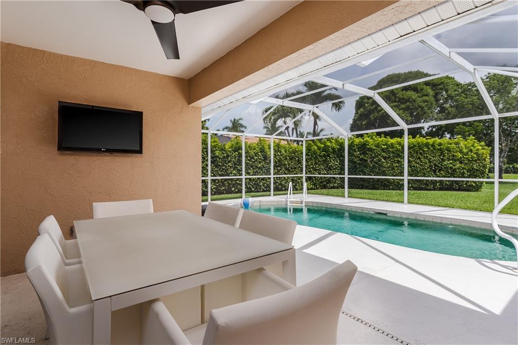 6658 Castlelawn Place, Unit 9 Naples, FL 34113 - Photo 27 of 38 Covered outdoor patio with a ceiling fan, wall-mounted television, and direct access to a screened-in pool area featuring a rectangular swimming pool, white deck, and surrounding manicured lawn with mature hedges