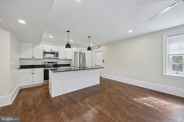 a large white kitchen with granite countertop a white stove top oven and white cabinets with wooden floor