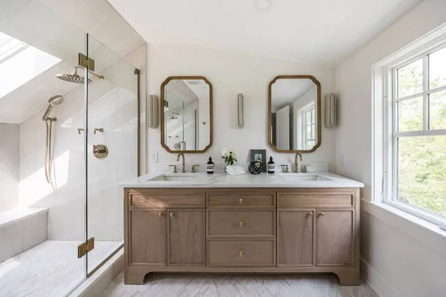 a en suite bathroom with double vanity a two sinks a large mirror a vanity a window and a bathtub