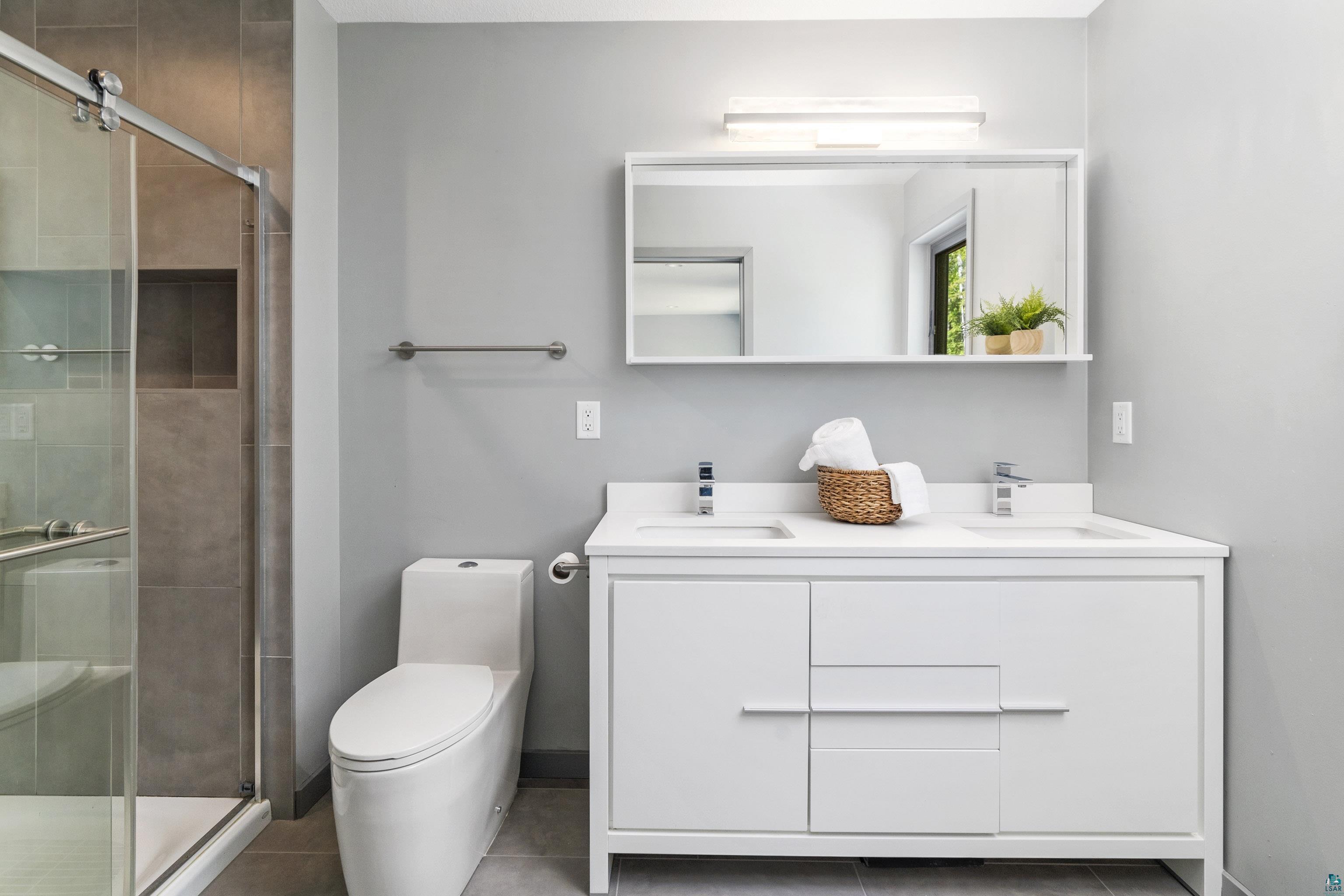 3625 London Road Duluth, MN 55804 - Photo 16 of 28 Bathroom featuring vanity with extensive cabinet space, toilet, tile floors, a shower with shower door, and double sink