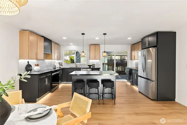 a kitchen with stainless steel appliances kitchen island granite countertop a refrigerator a sink a stove a dining table and chairs