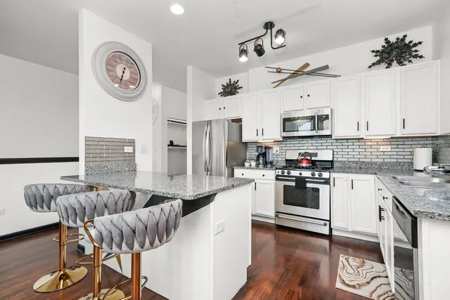 a kitchen with granite countertop a stove a sink dishwasher a dining table and chairs with wooden floor